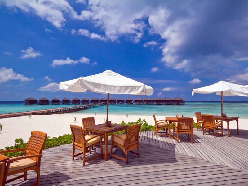 Strand mit Holzboden, Sonnenschirme, Stühlen und Tischen, türkisfarbenes Meer und blauer Himmel.