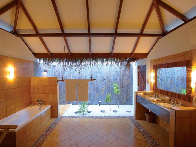 Geräumiges Bad mit Holzbalkendecke, Badewanne, großen Spiegeln und Blick auf Garten mit Steinen.