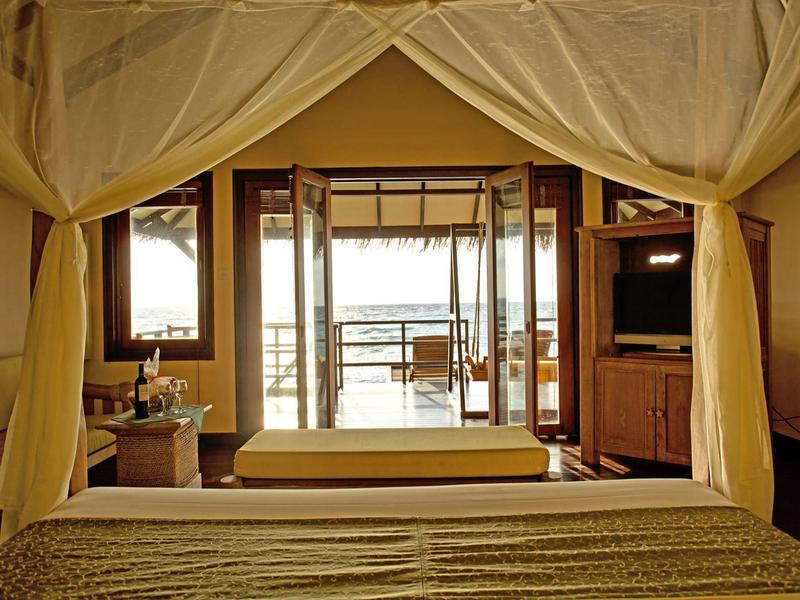 Gemütliches Schlafzimmer mit offener Tür zu Balkon und Sitzbereich, warme Farbtöne, bequeme Einrichtung.