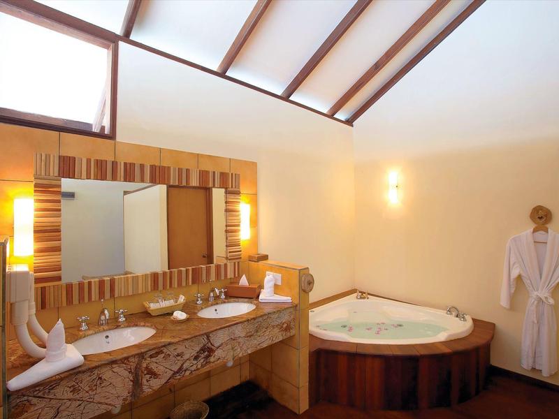 Helles Badezimmer mit Eckbadewanne, großem Spiegel und Holzdetails, zwei weißen Waschtischen und Sauna.