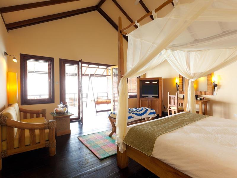 Gemütliches Schlafzimmer mit Himmelbett, Holzmöbeln und großem Fenster, das Tageslicht hereinlässt.