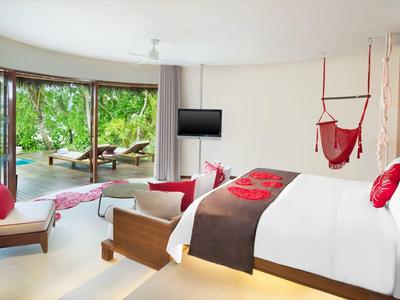 Helles Hotelzimmer mit großem Bett, roter Dekoration und Aussicht auf Garten und Meer.