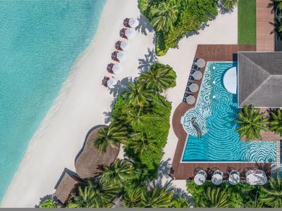 Luftaufnahme eines tropischen Resorts mit Pool, Palmen und weißem Sandstrand am türkisfarbenen Meer.