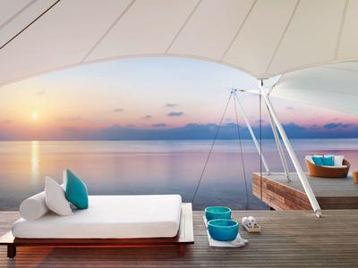 Moderní venkovní prostor s lehátkem, závěsnými sedadly a výhledem na západ slunce nad mořem.