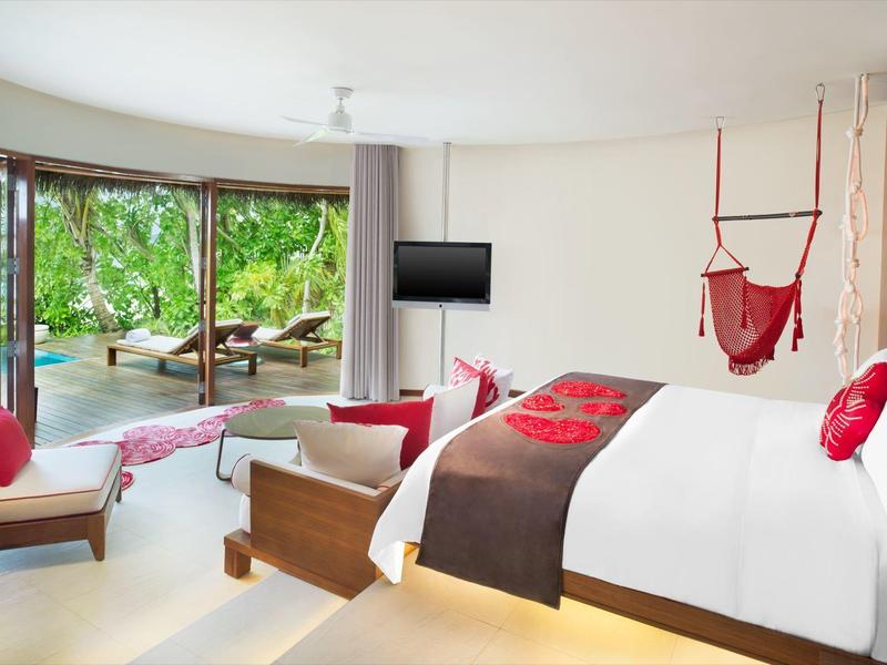 Helles Hotelzimmer mit großem Bett, roter Dekoration und Aussicht auf Garten und Meer.