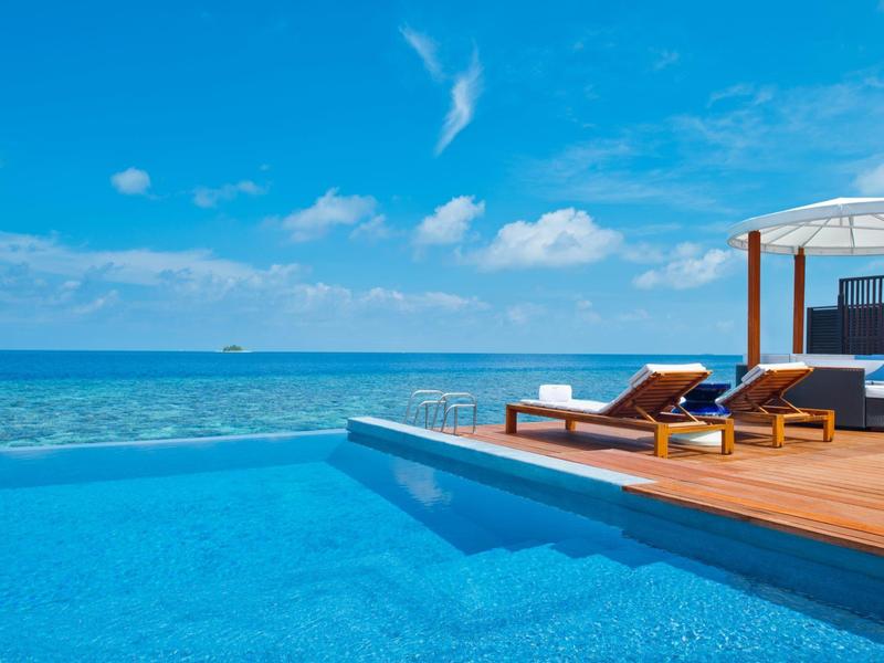 Infinity-Pool mit Meerblick und Sonnenliegen unter blauem Himmel