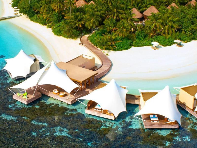 Luxuriöse Wasserbungalows mit weißen Segeldächern an einem tropischen Strand mit klarem Wasser.
