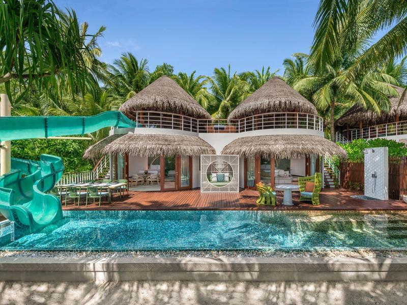 Moderner Pool mit Wasserrutsche und tropischen Palmen in einem Hotelresort.