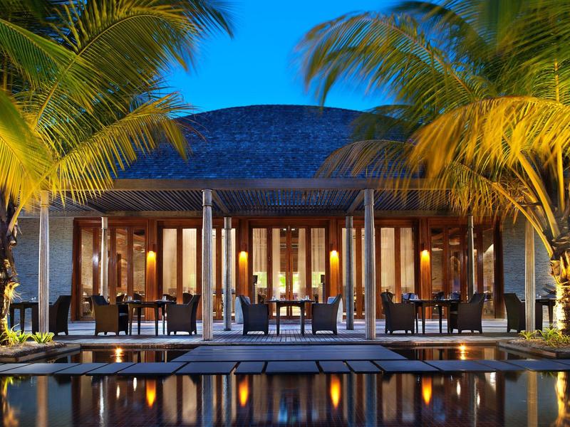 Beleuchtetes Resort mit Pool und Palmen bei Nacht unter klarem Himmel.