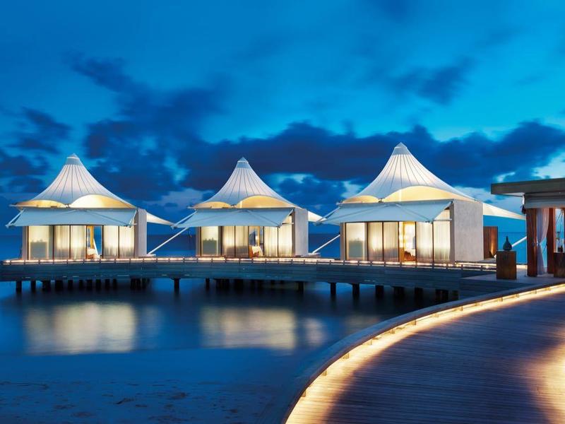 Bungalows auf Stelzen mit spitzen Dächern über Wasser bei Abenddämmerung