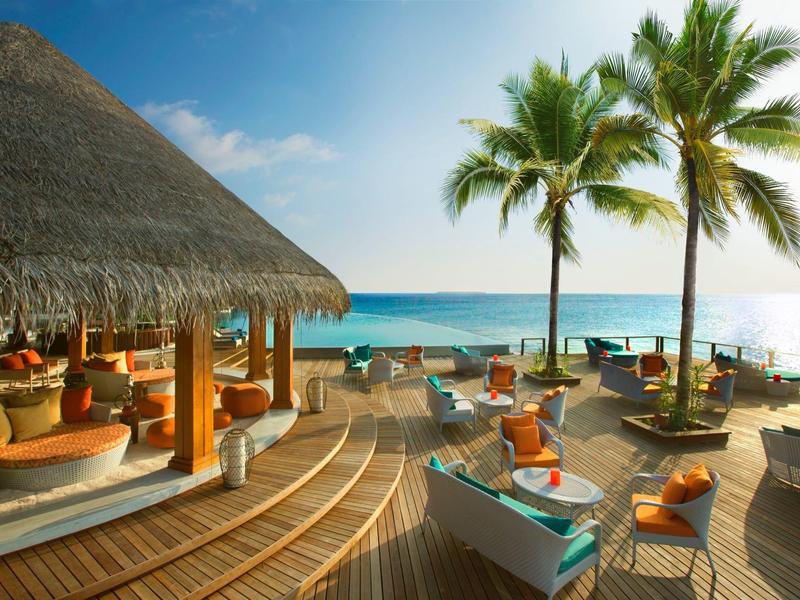 Strandhotel mit bequemen Sitzgelegenheiten und Palmen am Meer unter blauem Himmel.