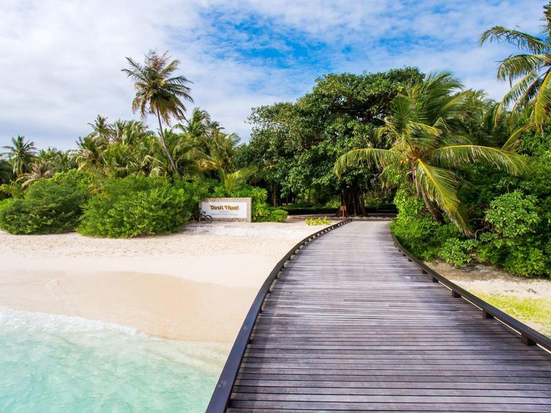 Holzsteg führt zu tropischem Strand mit Palmen und klarem Wasser.