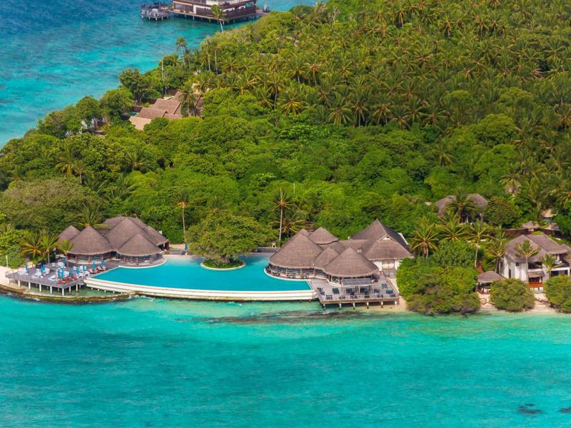 Luxuriöse Überwasserbungalows an einem tropischen Strand mit türkisfarbenem Wasser und dichter Vegetation.
