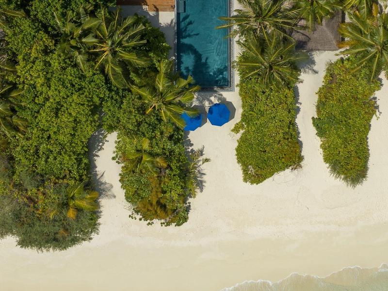 Vogelperspektive eines Pools neben einem weißen Sandstrand mit grünem tropischem Bewuchs.