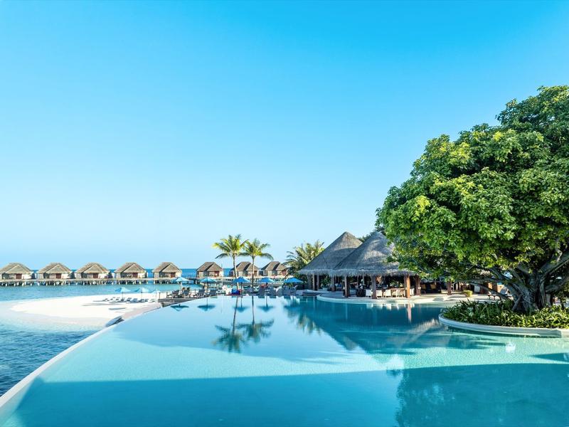 Infinity-Pool mit Blick auf das Meer und Strandhütten unter klarem Himmel
