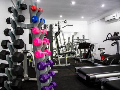 Salle de sport moderne avec haltères, tapis de course et machines dans une pièce lumineuse.