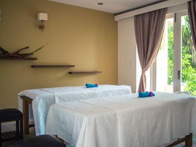 Zwei mit weißen Tüchern bedeckte Massageliegen in einem hellen Raum mit Vorhängen und natürlichem Licht.