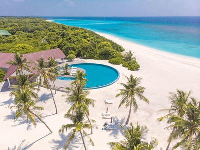 Strandresort mit rundem Pool, Palmen und weißem Sand am türkisblauen Meer.