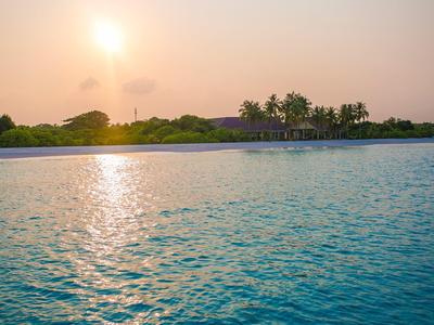Sonnenuntergang über einem ruhigen Pool mit Palmen und Gebäude im Hintergrund.