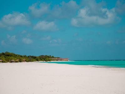 Weißer Sandstrand mit klarem blauem Wasser und bewölktem Himmel.