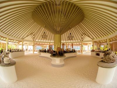 Großer offener Raum mit rundem Holzdeckendach und Sandboden, dekoriert mit Statuen.