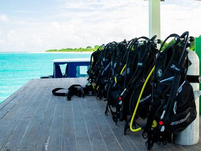 Plusieurs équipements de plongée alignés sur un quai au bord de la mer sous un ciel bleu.