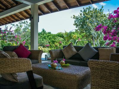 Gemütliche Lounge mit Rattanmöbeln und bunten Kissen auf einer Terrasse im Grünen.