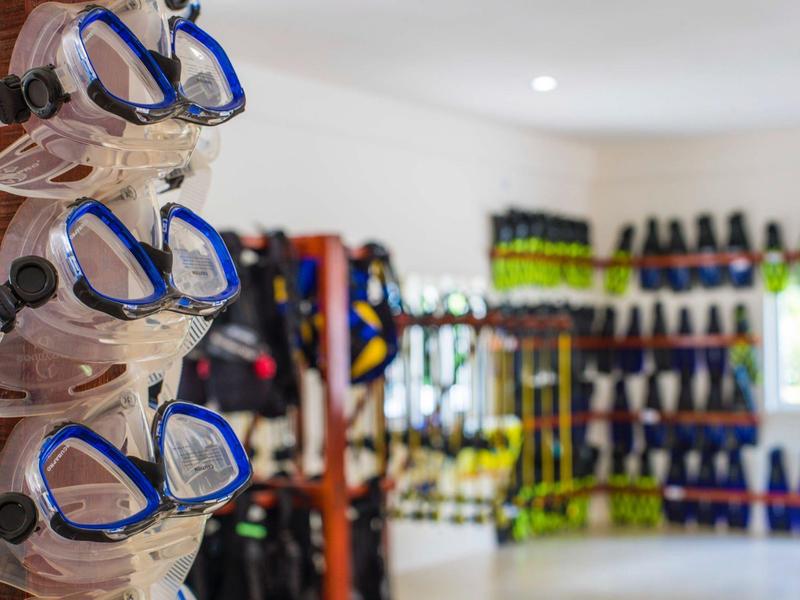 Mehrere Taucherbrillen hängen in einem belebten Taucherbedarfsladen mit Ausrüstung im Hintergrund.