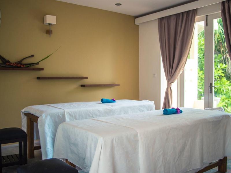 Zwei mit weißen Tüchern bedeckte Massageliegen in einem hellen Raum mit Vorhängen und natürlichem Licht.