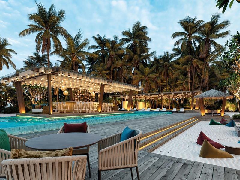 Ein tropisches Schwimmbad mit Sitzgelegenheiten und Palmen im Hintergrund.