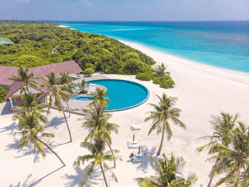 Strandresort mit rundem Pool, Palmen und weißem Sand am türkisblauen Meer.