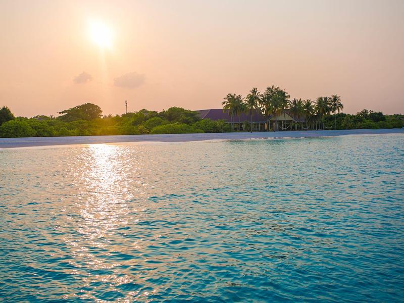 Sonnenuntergang über einem ruhigen Pool mit Palmen und Gebäude im Hintergrund.