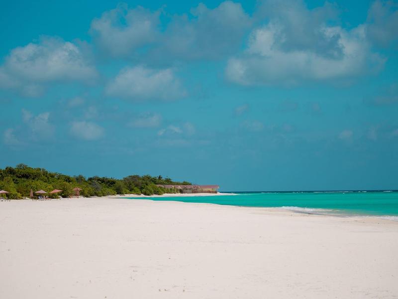 Weißer Sandstrand mit klarem blauem Wasser und bewölktem Himmel.