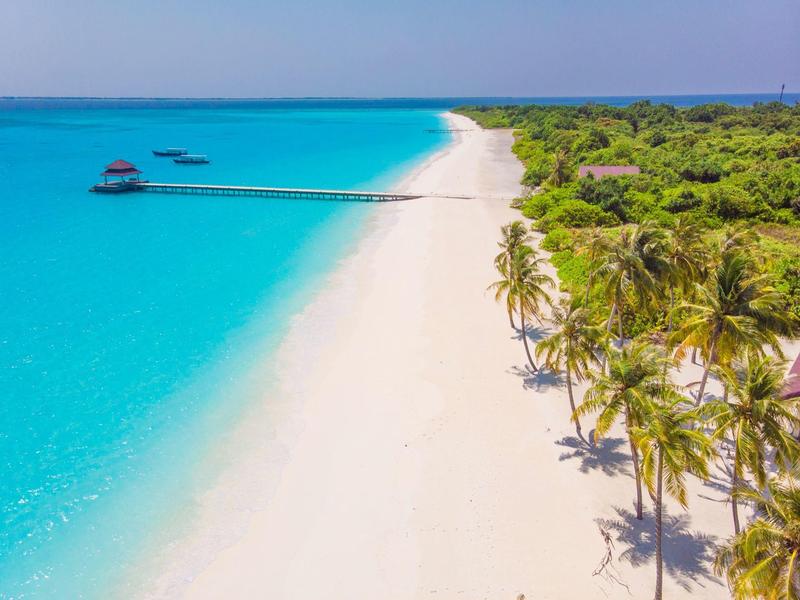 Weißer Sandstrand mit Palmen und Steg über türkisfarbenes Wasser