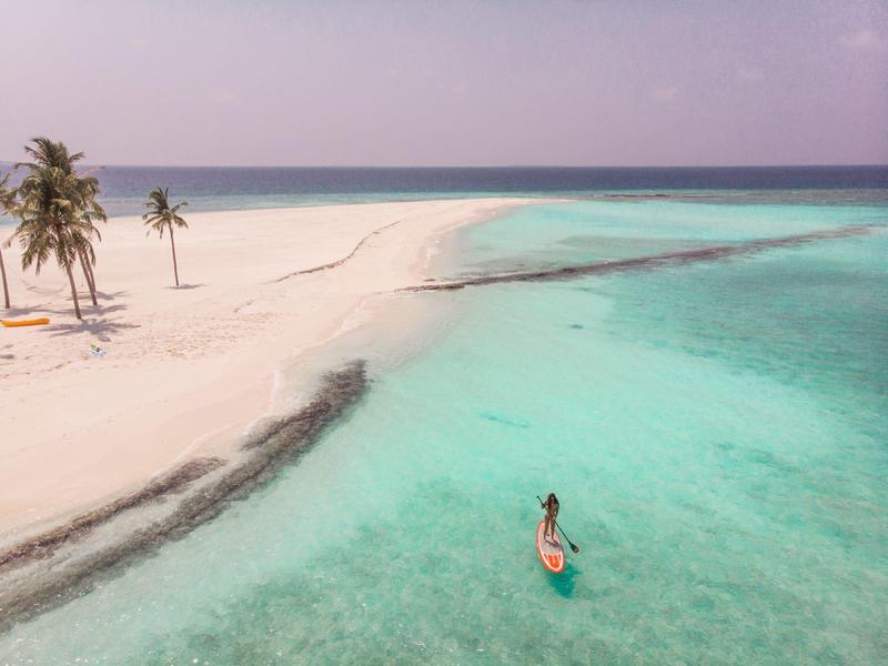 Klares türkisfarbenes Wasser trifft auf einen weißen Sandstrand mit wenigen Palmen.
