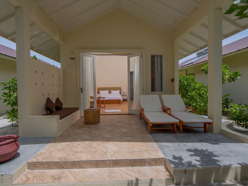 Helles, offenes Hotelzimmer mit Liegestühlen, Bett und Sitzbereich, umgeben von Natur.