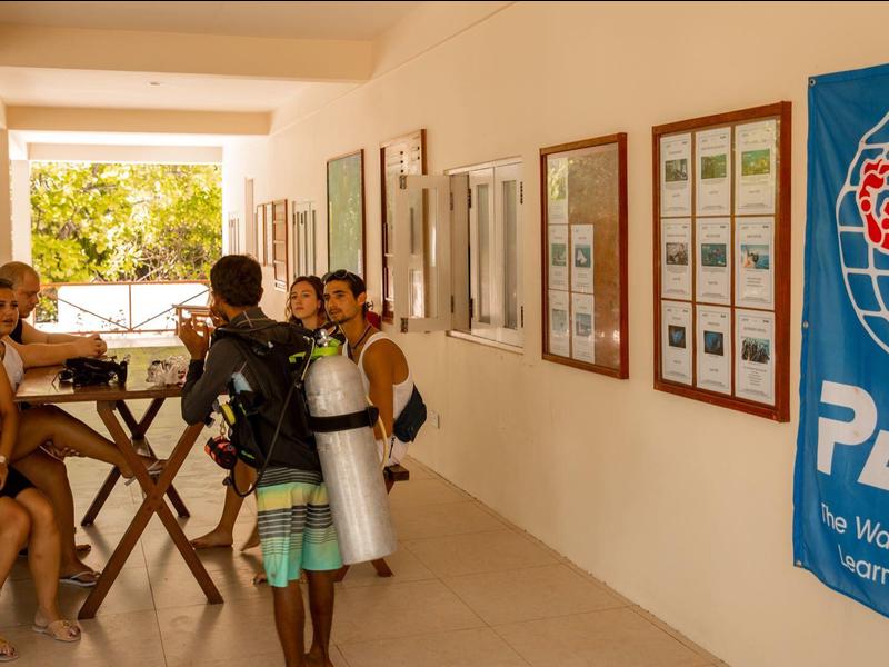 Kinder sitzen an einem Holztisch im Freien, ein Kind trägt Tauchausrüstung.