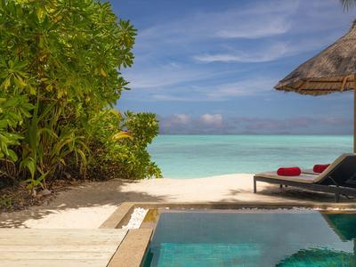 Basen z leżakami i widokiem na plażę oraz turkusowe morze pod błękitnym niebem.