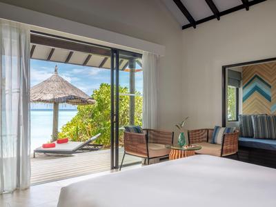 Widok z sypialni z otwartym balkonem na plażę z parasolem i leżakami.