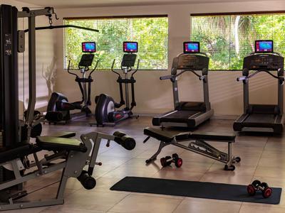 Siłownia z bieżniami, rowerami stacjonarnymi, hantlami i matą do ćwiczeń przed dużymi oknami.
