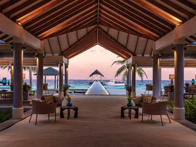 Otwarta przestrzeń hotelowa z widokiem na basen i plażę o zachodzie słońca.