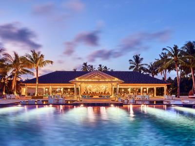 Hotel z oświetlonym basenem i palmami o zachodzie słońca na tropikalnej plaży