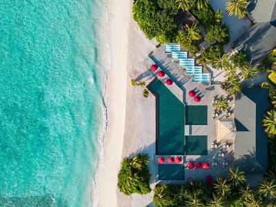 Zdjęcie z lotu ptaka ośrodka nadmorskiego z niebieskimi leżakami i czerwonymi parasolami obok turkusowej wody.