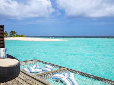 Słoneczny taras z leżakami z widokiem na turkusowe morze i piaszczystą plażę.