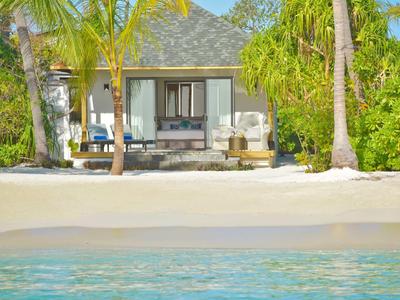 Villa sulla spiaggia con palme, sabbia e vista sull'acqua limpida del mare.