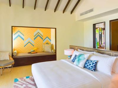 Modern furnished bedroom with large bed, seating area, and colorful wall decoration.