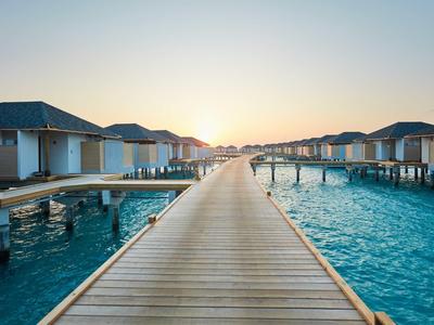 Lungo percorso in legno tra bungalow sull'acqua al tramonto su acque limpide e blu.