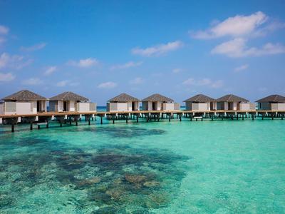 Bungalow su palafitte sopra acqua turchese limpida con cielo blu e alcune nuvole.