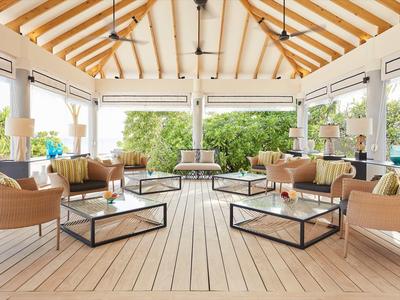 Area lounge aperta e luminosa con mobili moderni e pavimento in legno sotto un tetto in assi di legno.