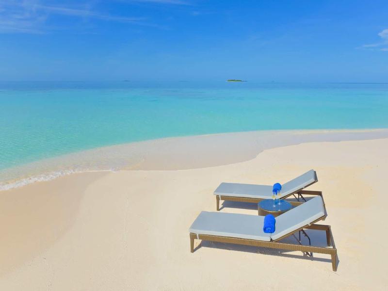 Due sdraio con bottiglie d'acqua blu sulla tranquilla spiaggia di sabbia bianca sotto un cielo azzurro.